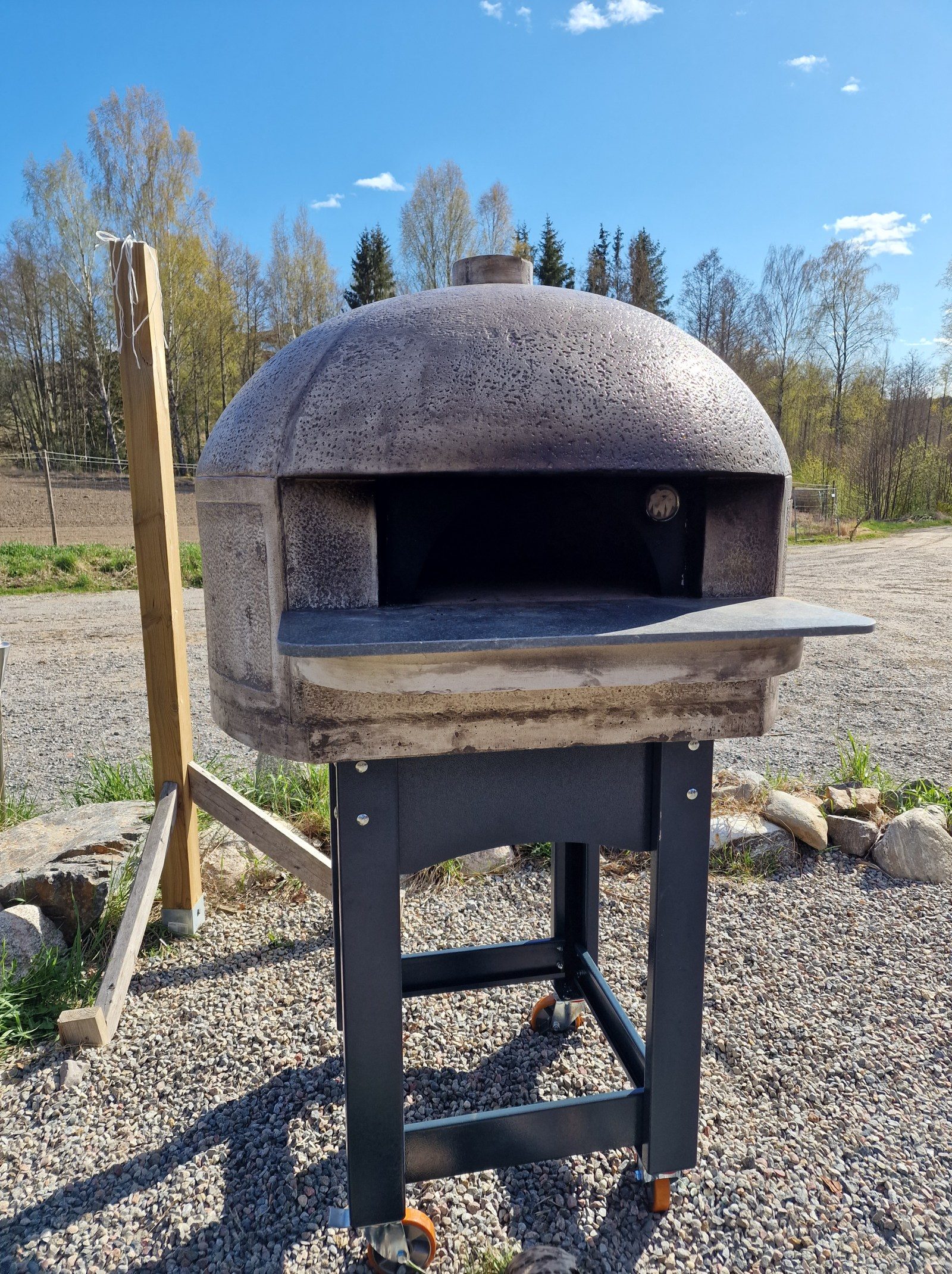 Marcus eldar en vedugn på ett pizzaevent i en trädgård medan gästerna väntar på färsk pizza.