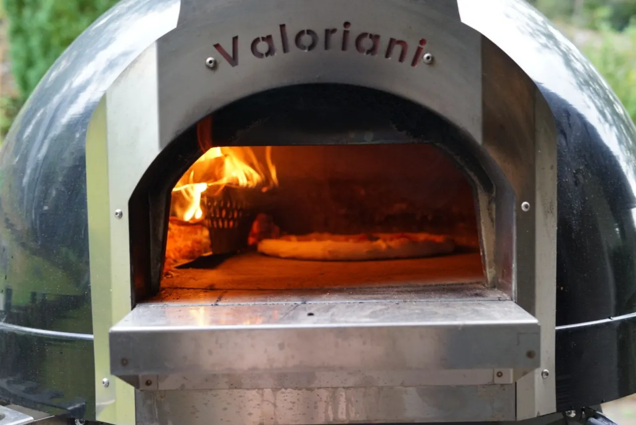 En pizza gräddas i en vedeldad Valoriani-ugn med lågorna dansande intill.